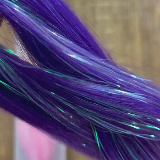 Close up look at purple pink girls extension braids with tinsel woven through over wood background.