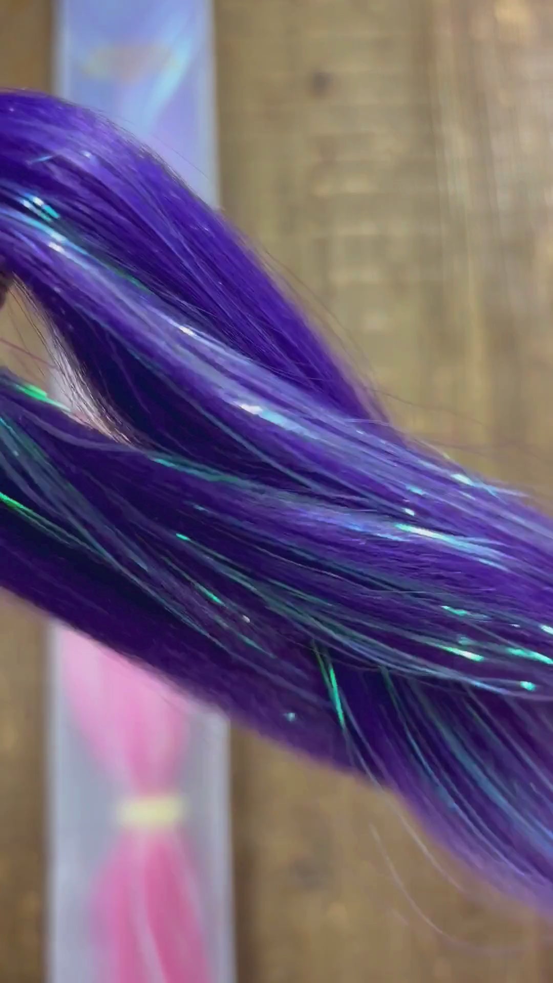 Close up look at purple pink girls extension braids with tinsel woven through over wood background.