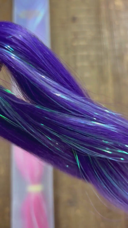 Close up look at purple pink girls extension braids with tinsel woven through over wood background.