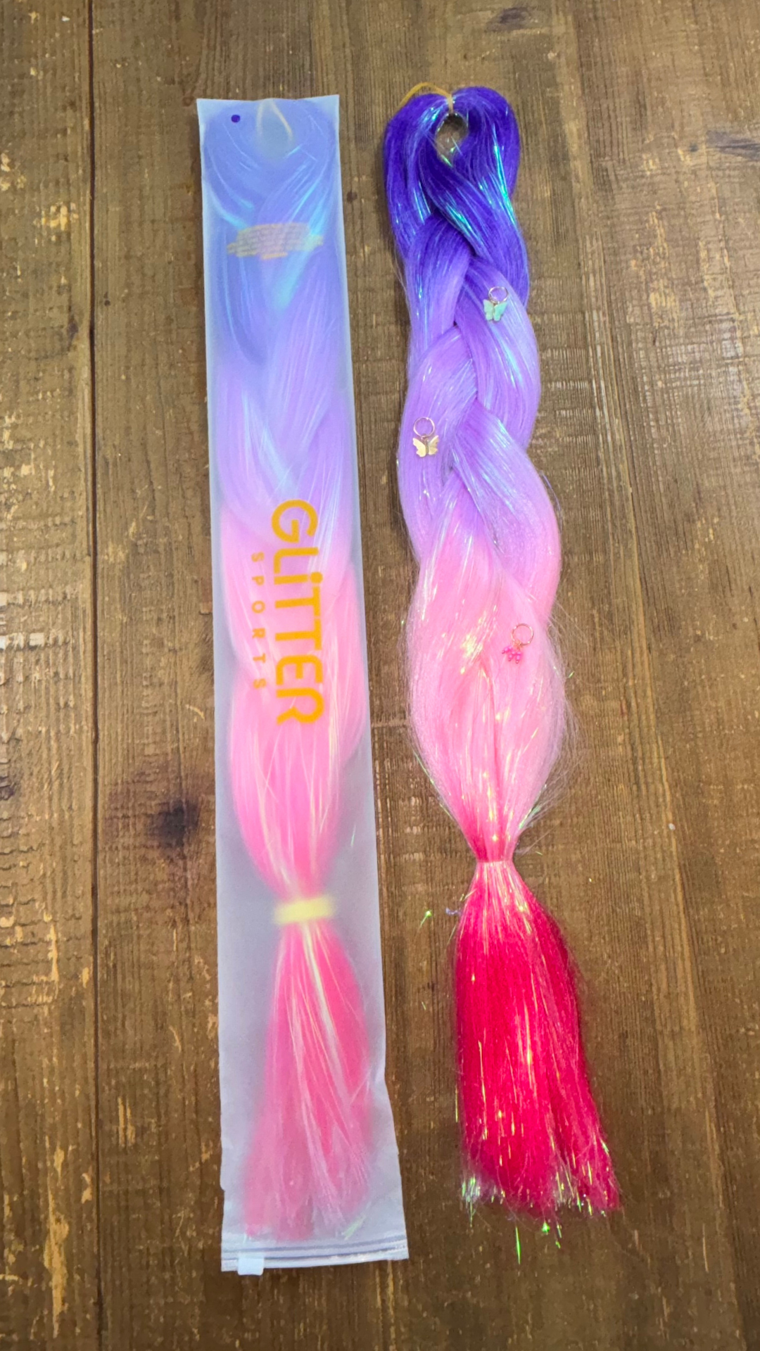 Purple and pink ombre girls Disney princess hair extension braids with butterfly hair charms on wood background.